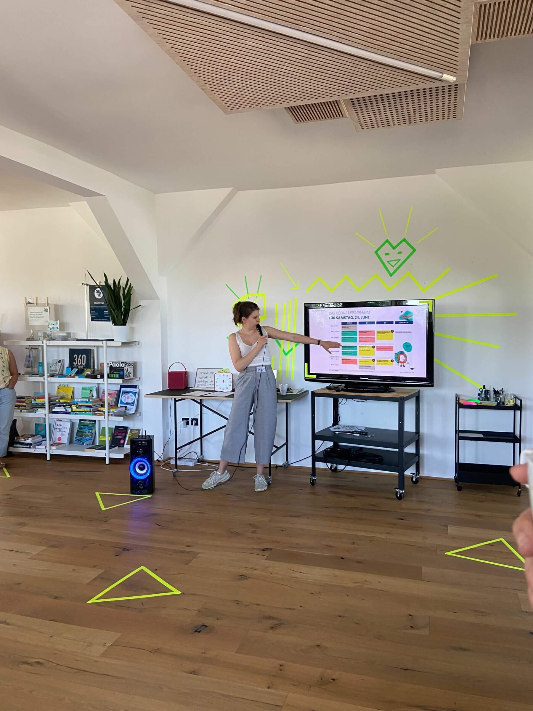 Foto der KOON23 mit einer Frau, die auf eine Präsentation auf einem TV zeigt