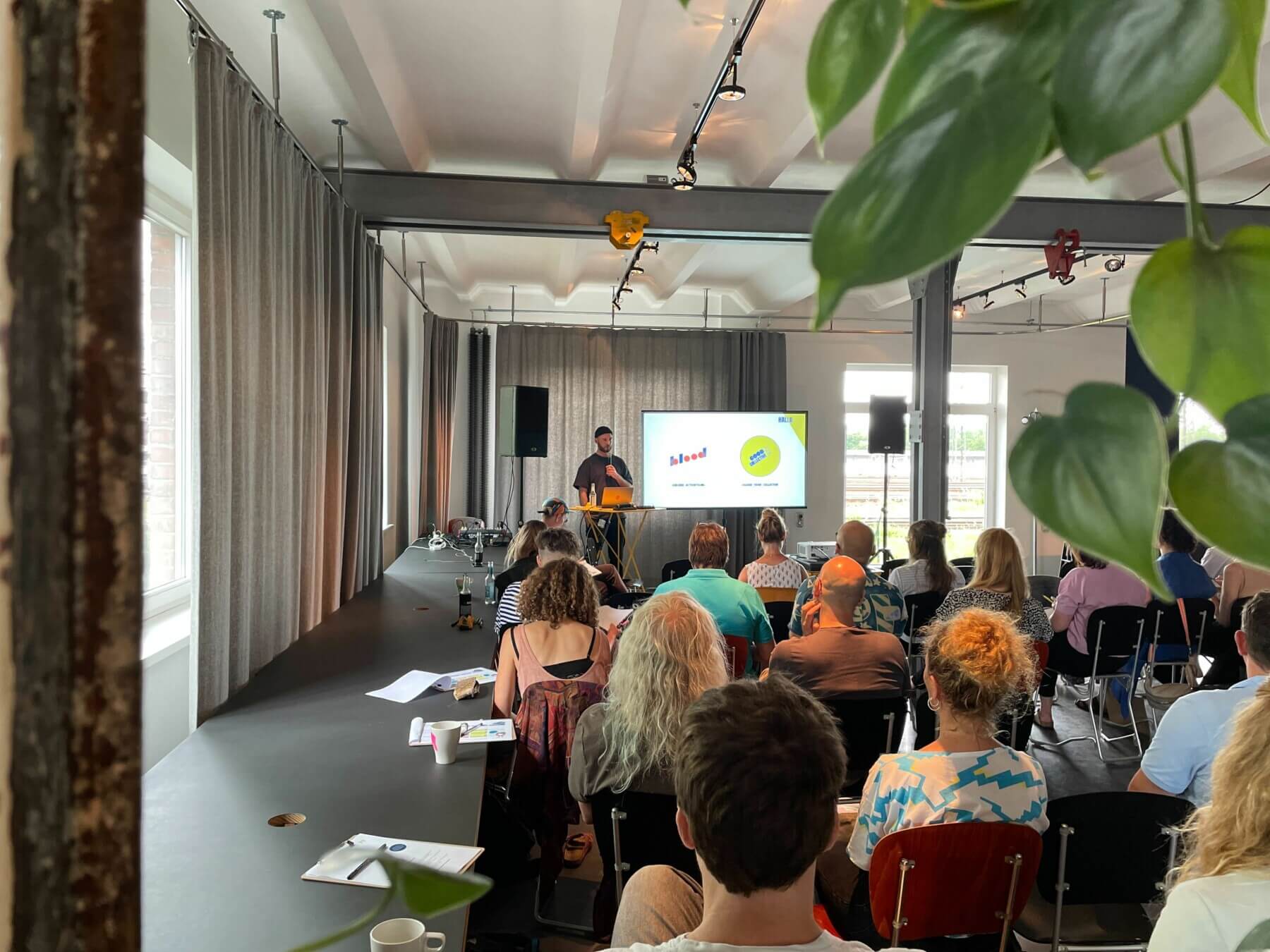 Beispielfoto für einen Impuls auf der KOON23 mit Menschen, die auf Stühlen sitzen und einem Vortragenden zuhören