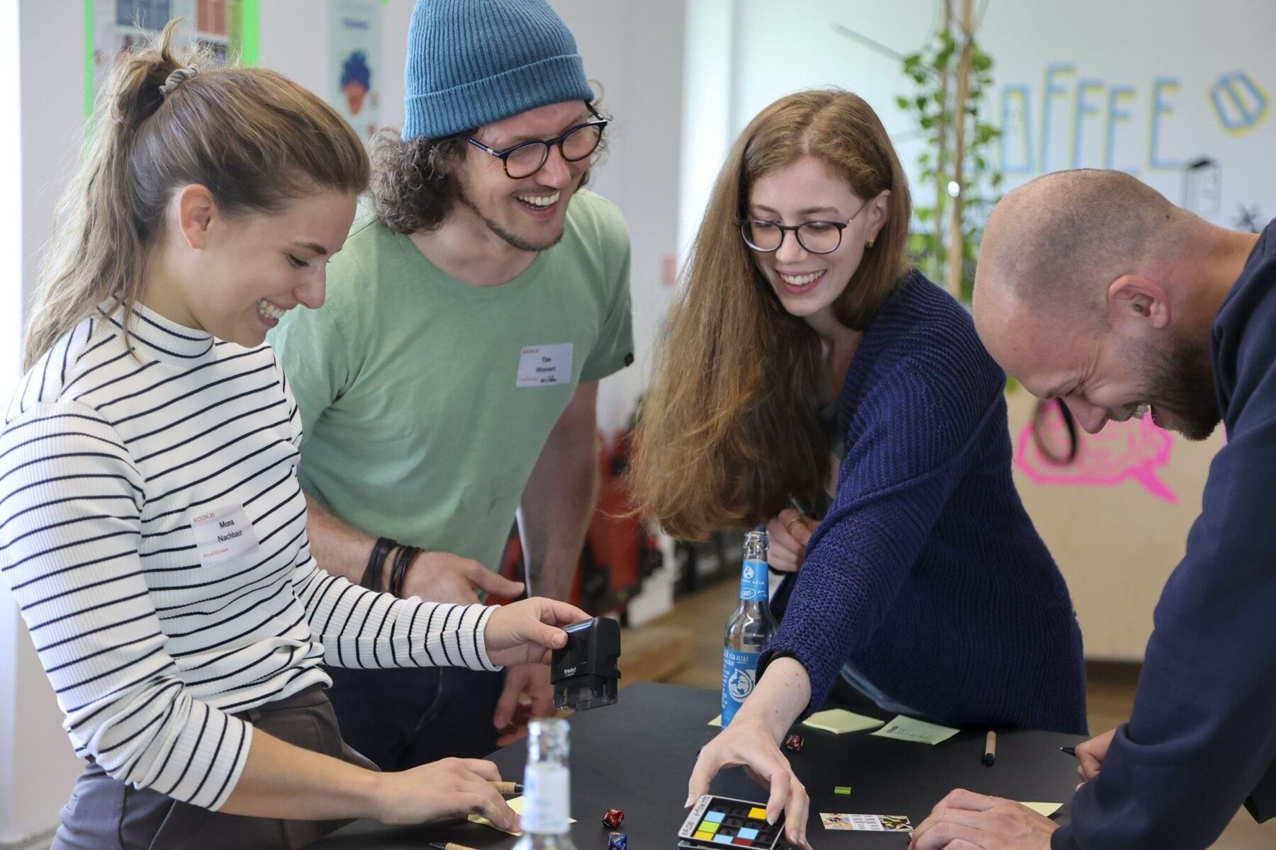 Vier Teilnehmende eines Workshops lachen und interagieren an einem Tisch mit Spielmaterialien